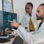Dois profissionais de saúde de bata branca a analisar imagens médicas digitais em monitores
