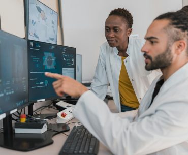 Dois profissionais de saúde de bata branca a analisar imagens médicas digitais em monitores