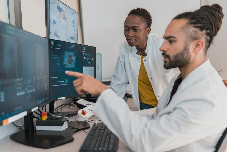 Dois profissionais de saúde de bata branca a analisar imagens médicas digitais em monitores